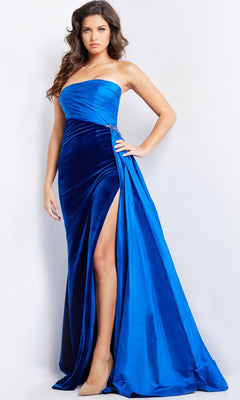 A woman wearing a strapless long prom dress with side sash in royal blue velvet and a high slit stands against a light background.