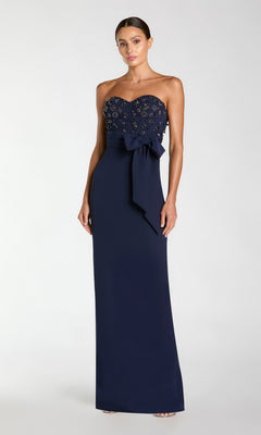 A woman stands against a plain light background wearing the Mac Duggal 2395 Long Formal Dress in Midnight, featuring a strapless design with bead embellishments on the bodice and a bow at the waist.