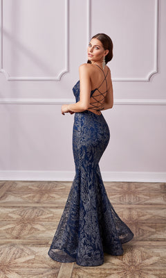 A woman in the Long Navy Glitter Prom Dress: Aerie Couture 239, featuring a lace pattern and crisscross straps, stands on a wood floor and looks over her shoulder.