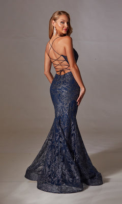 Woman wears the Long Navy Glitter Prom Dress: Aerie Couture 239, featuring a fitted bodice, floor-length lace skirt, open back with crisscross straps, as she stands on a plain backdrop and looks over her shoulder.