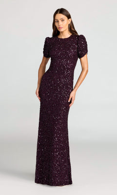 A woman wears the Mac Duggal 24003 Short Sleeve Sequin Formal Dress in Blackberry, featuring puffed sleeves and a floor-length silhouette, set against a plain background.