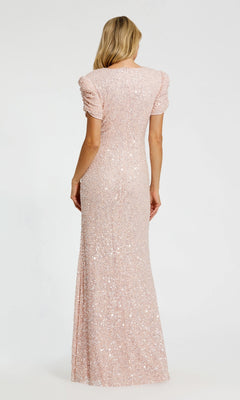A blonde woman, seen from the back against a plain light background, wears the Mac Duggal 24003 Short Sleeve Sequin Formal Dress in light pink, a floor-length formal gown.