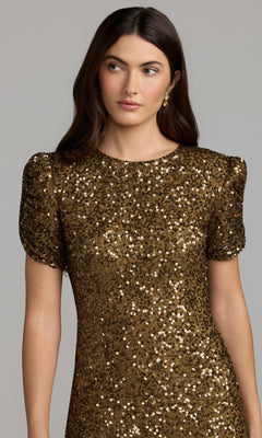A woman wears the Mac Duggal 24003 Short Sleeve Sequin Formal Dress in gold, featuring short puff sleeves, as she stands against a plain light gray background.