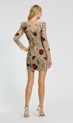 A woman stands facing away, wearing the Short Party Dress: Mac Duggal 24006—a fitted nude mini dress with long sleeves, embellished with colorful beaded floral embroidery, and elegantly paired with gold high-heeled sandals.