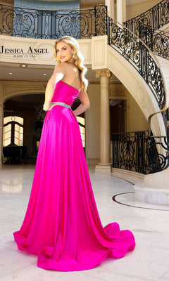 A woman wearing the Strapless High-Low Prom Dress: Jessica Angel 2402 in vibrant pink stands in an elegant foyer with a grand staircase and ornate railing in the background.