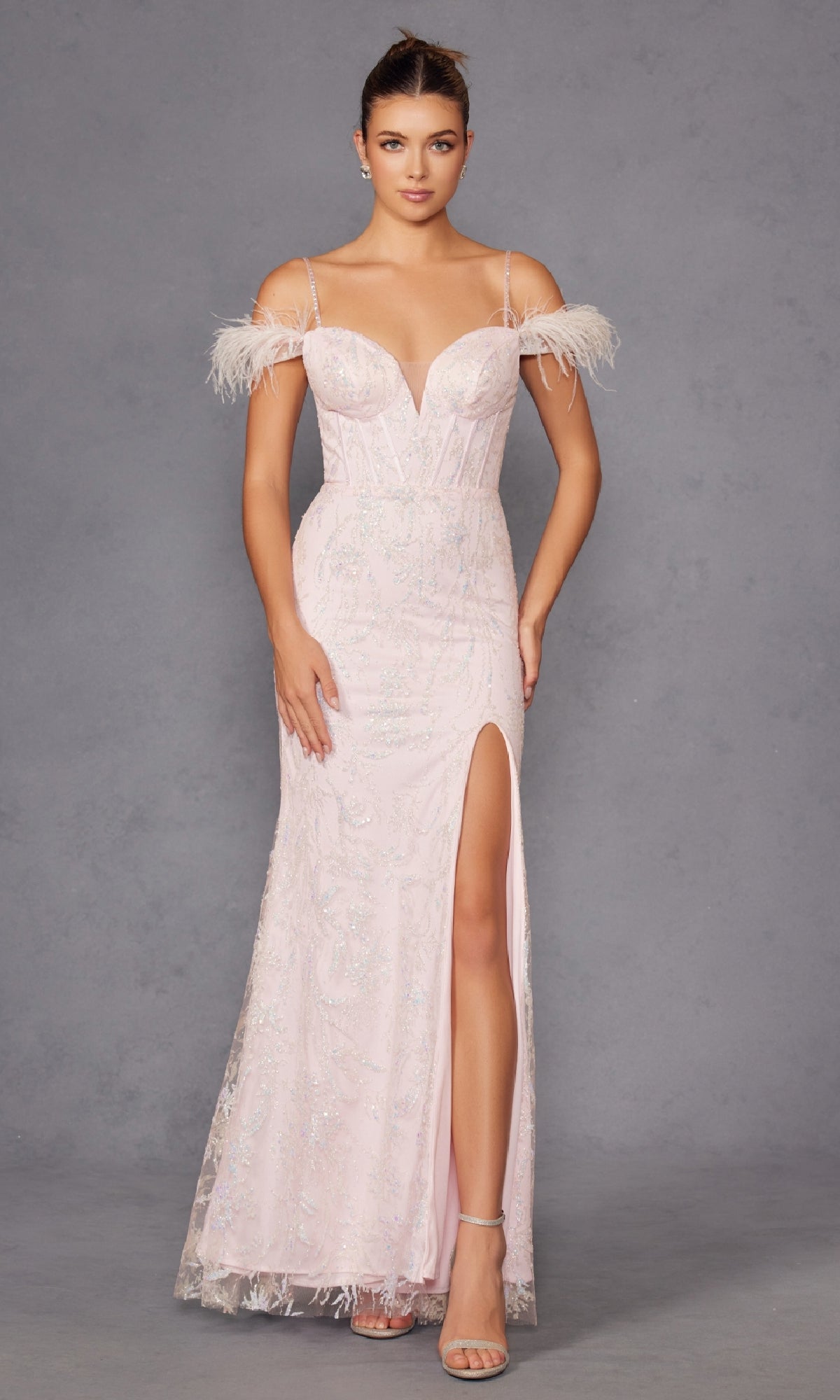 A woman models the Feather Cold-Shoulder Long Glitter Prom Dress 2402, featuring feathered straps, a light pink hue, glitter details, and a thigh-high slit.