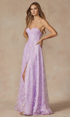 A woman wears the Juliet 2403 Long Prom Dress—a strapless, floor-length lavender gown with a corset bodice, subtle floral lace pattern, and front slit—while standing against a neutral background.