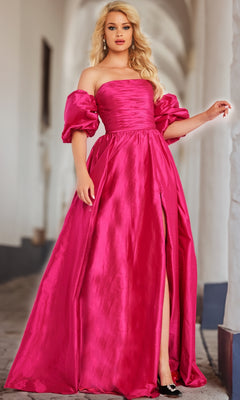 A woman in the Jovani Puff-Sleeve Long Prom Ball Gown 24099, a bright pink formal dress with puff sleeves and a thigh-high slit, stands in a corridor with white arches.