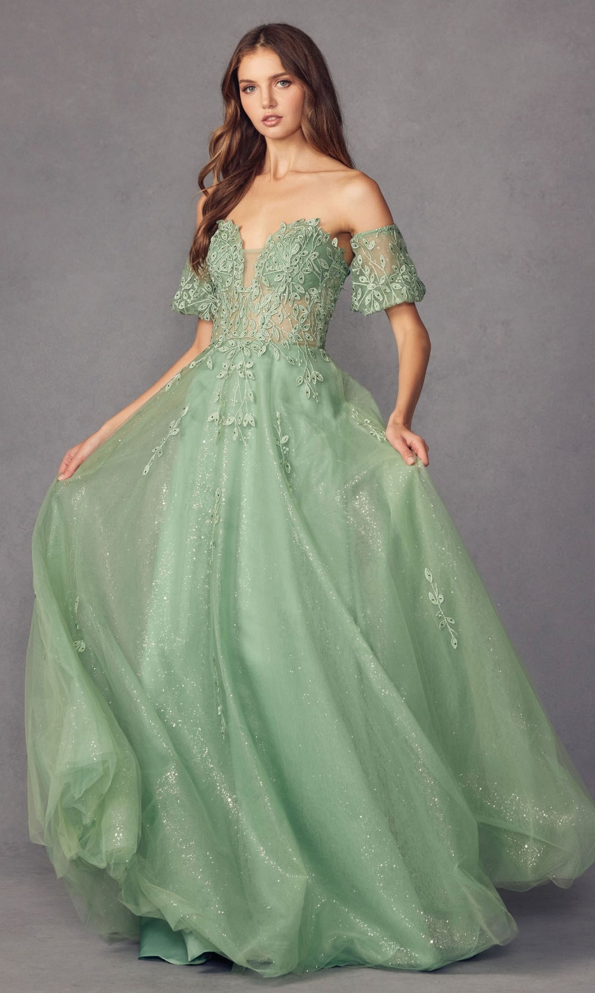 A woman wearing the Puff-Sleeve Strapless Glitter Prom Ball Gown 2409 stands against a plain gray background. The floor-length gown features detachable puff sleeves, sparkling mint green fabric, and intricate floral embroidery.