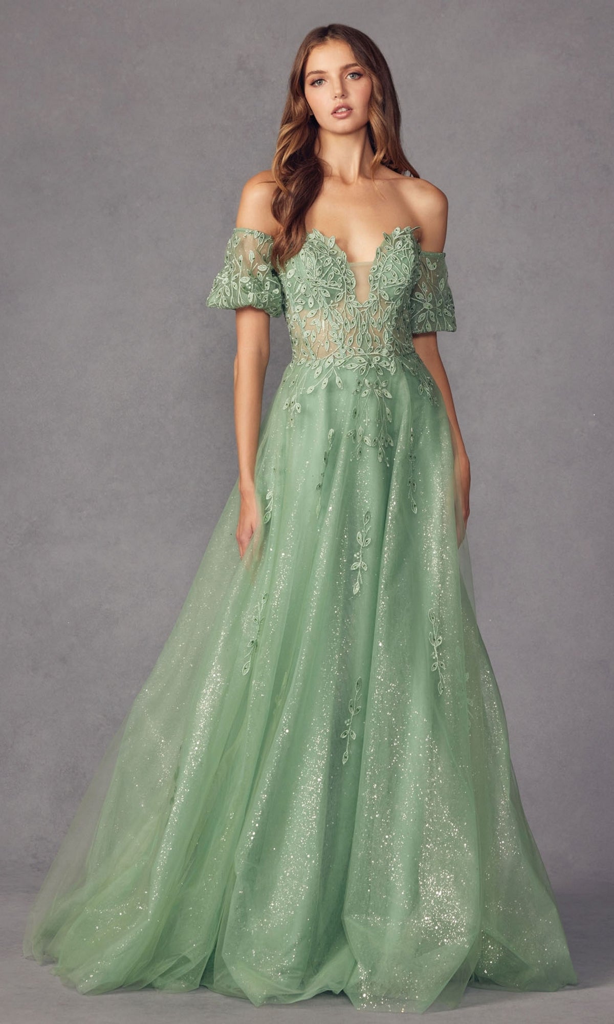A woman models the Puff-Sleeve Strapless Glitter Prom Ball Gown 2409, featuring a light green hue, detachable puff sleeves, sheer embroidered details, and a sparkling tulle skirt against a neutral backdrop.