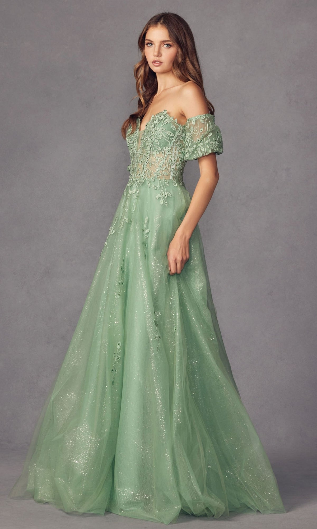 A woman wears the Puff-Sleeve Strapless Glitter Prom Ball Gown 2409—a light green, floor-length gown with a fitted bodice, sheer fabric, floral embroidery, and detachable puff sleeves.