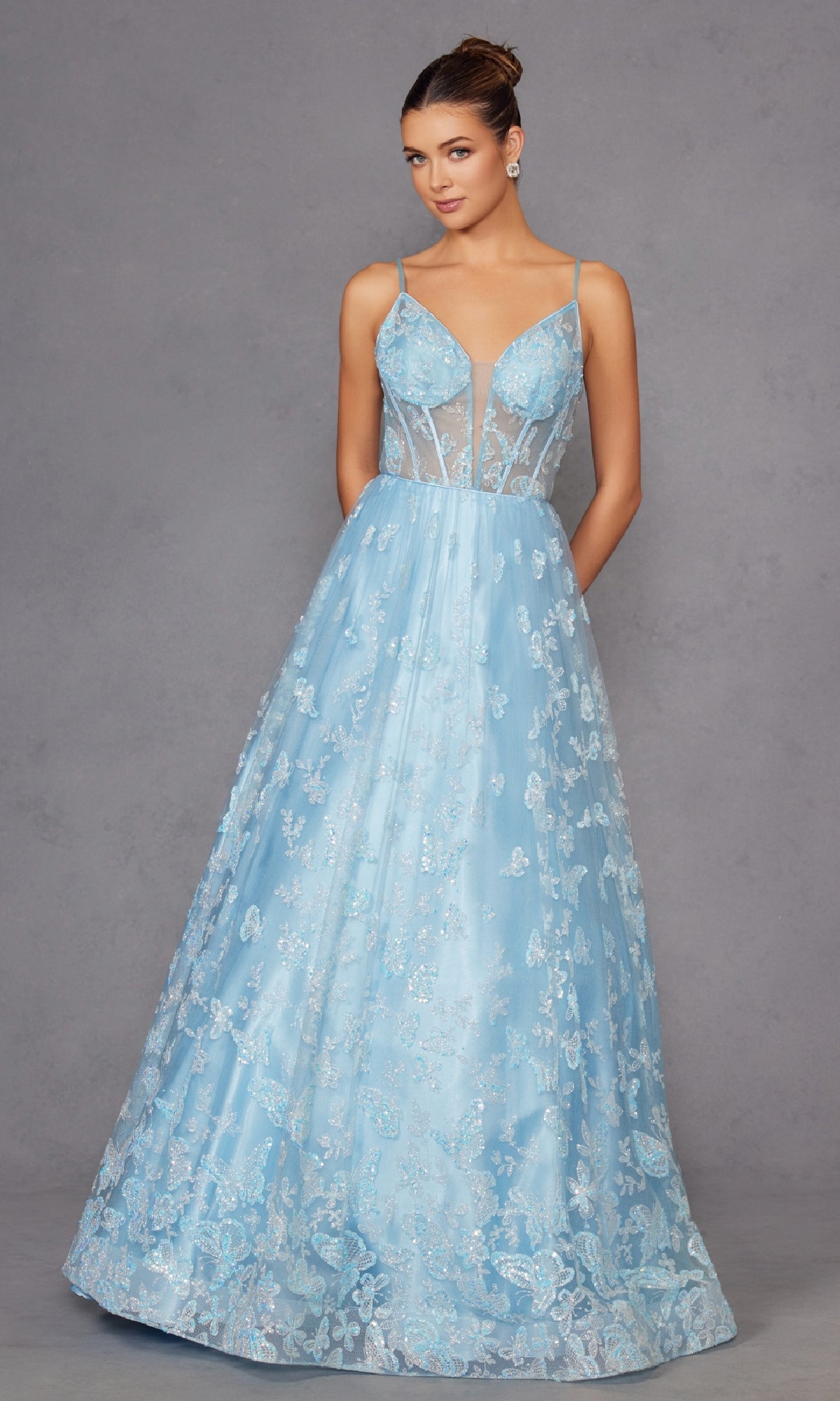 A woman stands against a gray background wearing the Sheer-Corset Glitter-Print Long Prom Dress 2413, featuring thin straps, a floor-length a-line silhouette, and a sheer bodice with sparkling details.