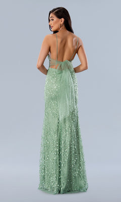 A woman is wearing the Long Prom Dress 24185 by Stella Couture, a light green beaded formal gown with thin straps, a sheer bow, and an open back, standing against a plain light gray background.