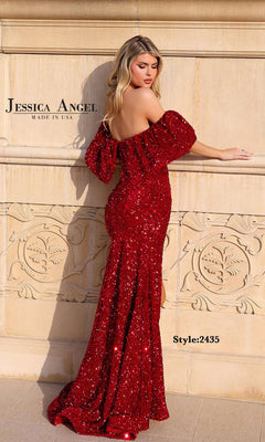 A woman poses outdoors against a stone wall wearing the Bow Long Sequin Prom Dress by Jessica Angel (Style 2435), a fitted, floor-length red gown with shimmering sequins and an off-the-shoulder design.