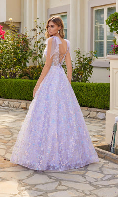 A woman wearing the Juliet JT2439K Lilac Purple Long Lace Prom Dress stands outdoors on a stone path near a garden and white building.