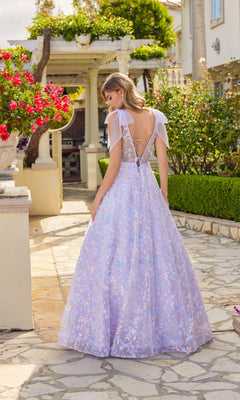 A woman wearing the Juliet JT2439K Lilac Purple Long Lace Prom Dress stands outdoors on a stone path, surrounded by greenery and flowers.