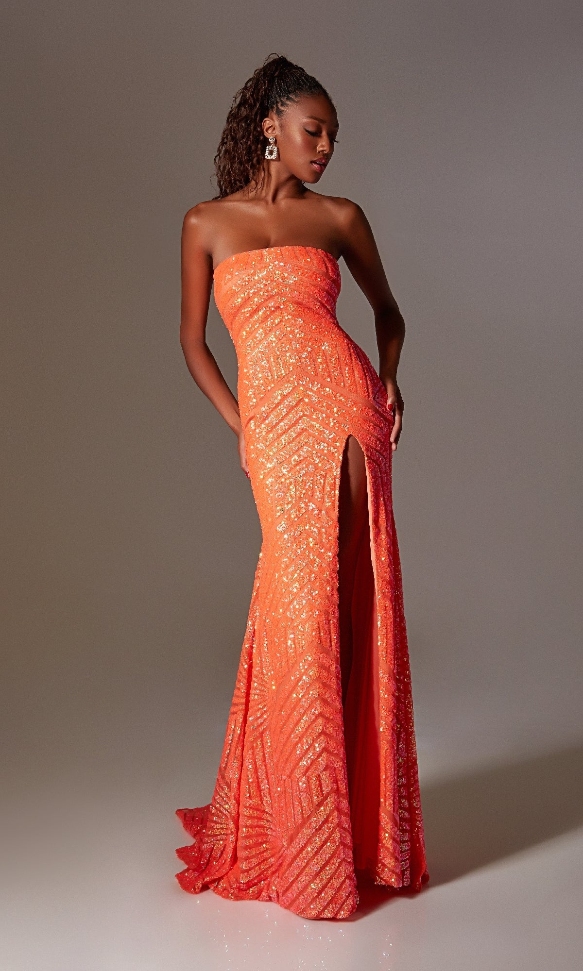 A woman models the Strapless Long Sequin Prom Gown: Aerie Couture 243, an orange, floor-length dress with a high slit and strapless design, standing against a plain background and gazing slightly to the side.