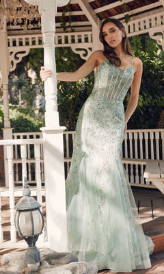 A woman wearing the Juliet JT2441S Long Sequin Mermaid Prom Dress in light green with thin straps stands in a gazebo, resting one hand on a white pillar.