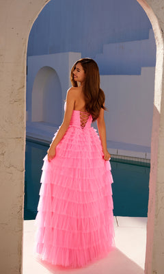 A woman wearing the Long Prom Dress JT2456H by Juliet, a strapless ball gown with ruffle tulle layers, stands under an archway near a pool, facing away from the camera.
