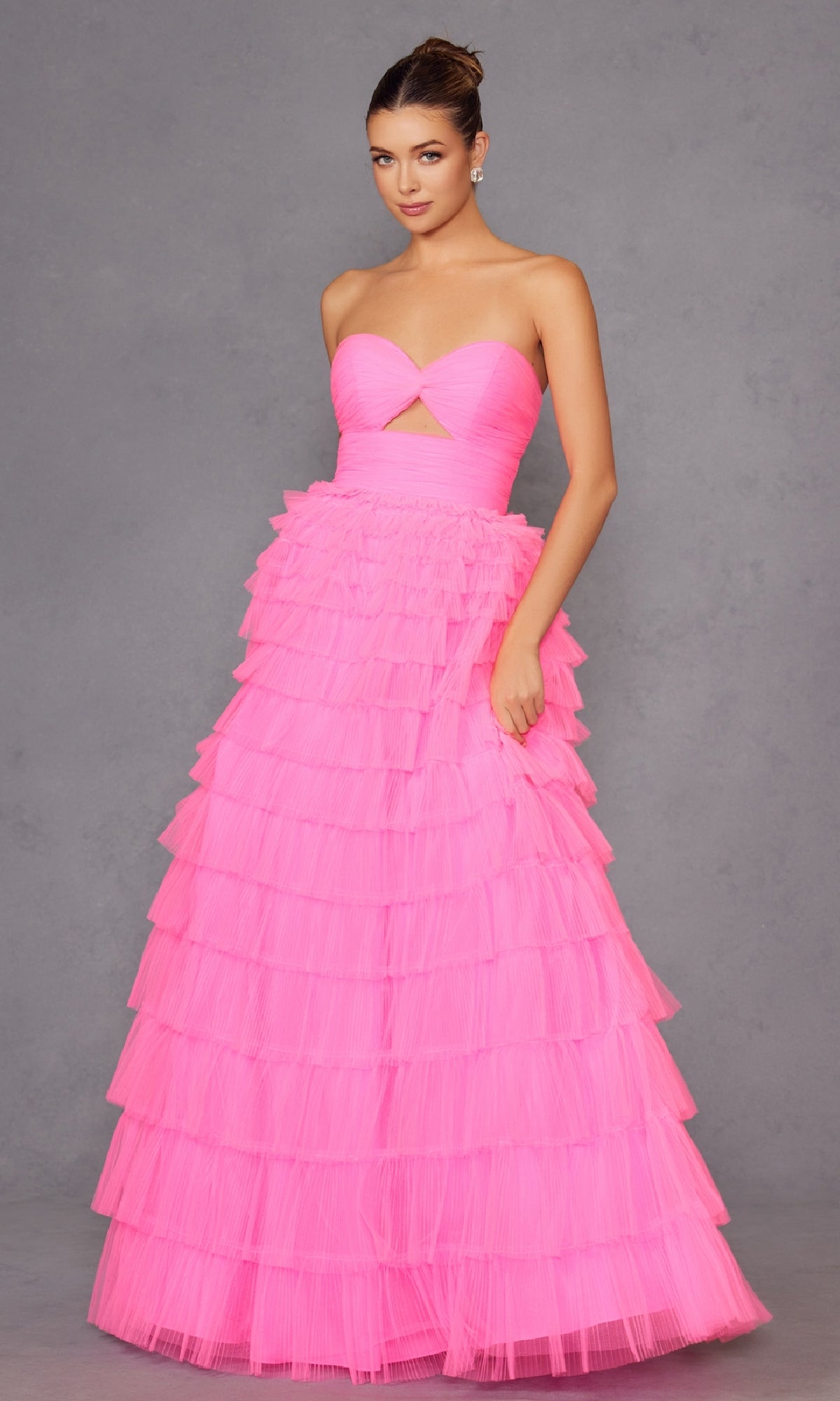 A woman wears the Long Prom Dress JT2456H by Juliet, a strapless ball gown with an empire waist and ruffle tulle tiered skirt, standing against a plain gray background.