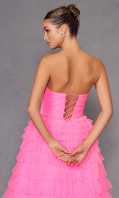 A woman wearing the Long Prom Dress JT2456H by Juliet—a strapless, bright pink tiered ruffle tulle gown with lace-up back and empire waist—stands against a gray backdrop, hands clasped behind her.