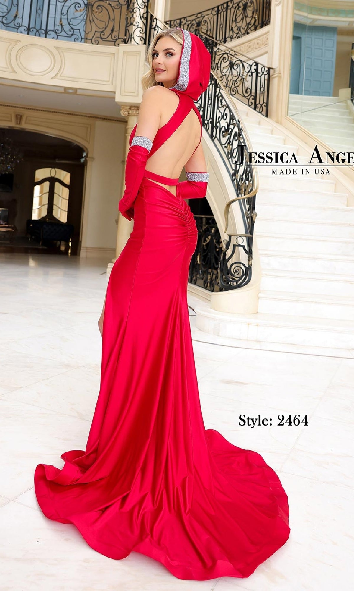 A woman wearing the Gloved Long Hooded Prom Dress: Jessica Angel 2464, featuring a backless design and silver trim, stands indoors near a staircase, glancing over her shoulder.