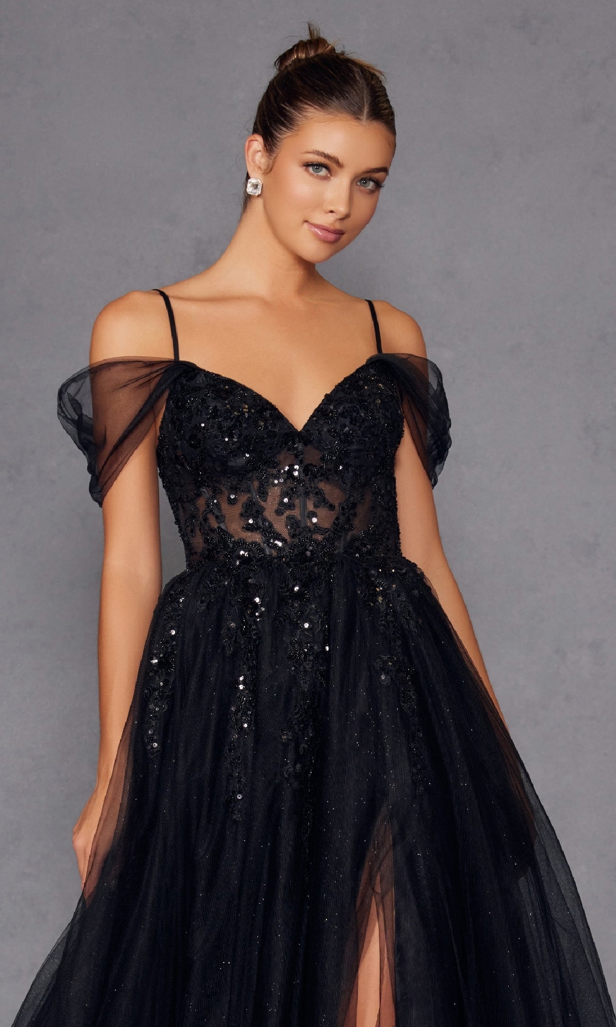 A woman models the Sheer-Waist Long Prom Ball Gown (Juliet JT2466A), a black off-the-shoulder dress with thin straps and sequin details, posing gracefully against a plain gray background.