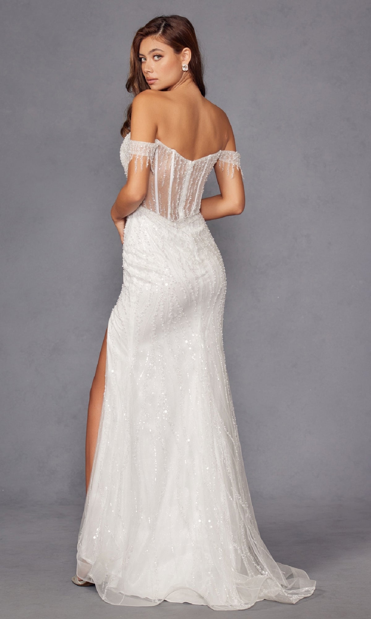 A woman wears the Long Prom Dress JT2471LW by Juliet, featuring sequins, an off-the-shoulder neckline, sheer illusion bodice, fitted silhouette, and high slit, standing against a plain gray background.