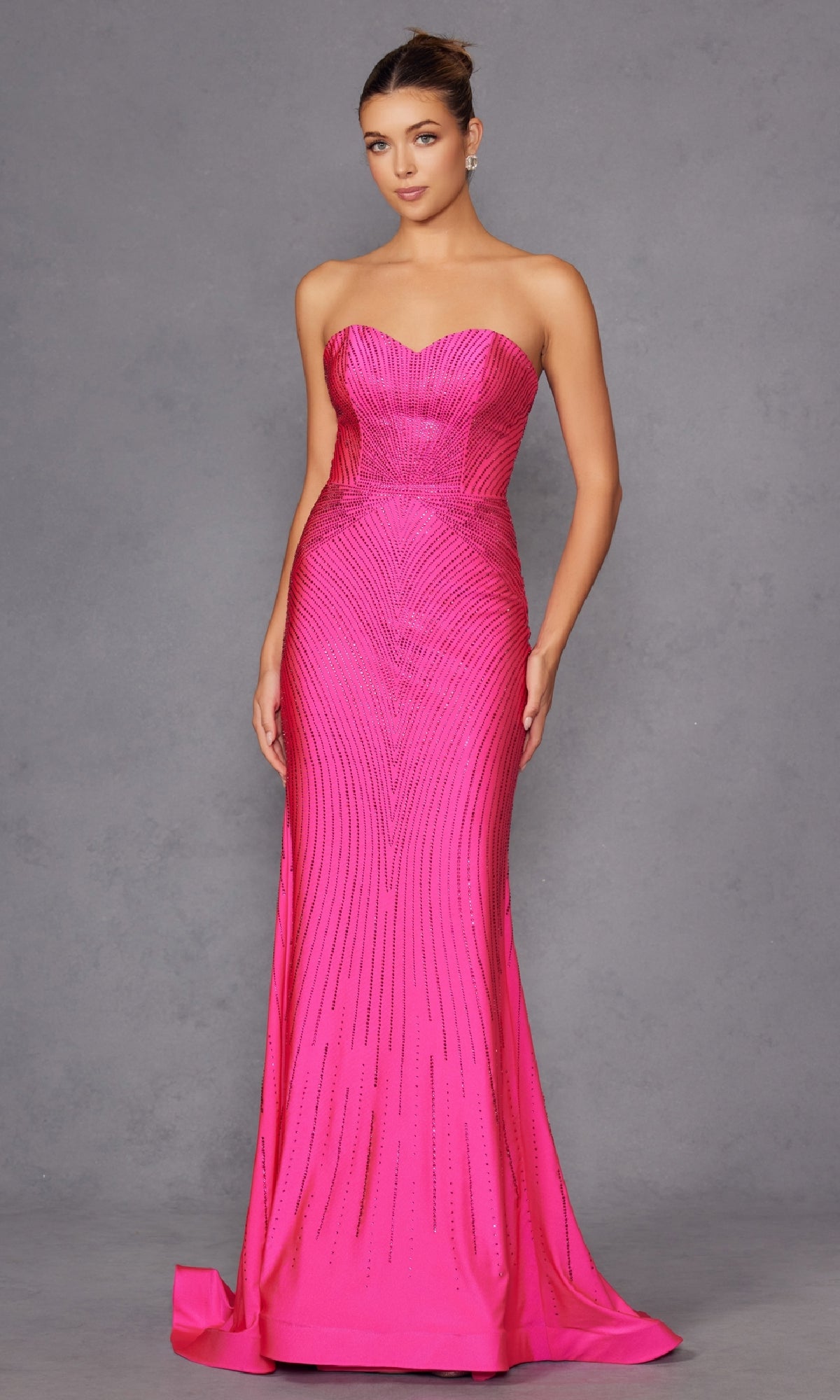 A woman poses against a plain gray background in the Strapless Long Sequin Prom Dress: Juliet JT2472R—a fitted, floor-length hot pink gown featuring a subtle linear pattern and an elegant sweetheart neckline.
