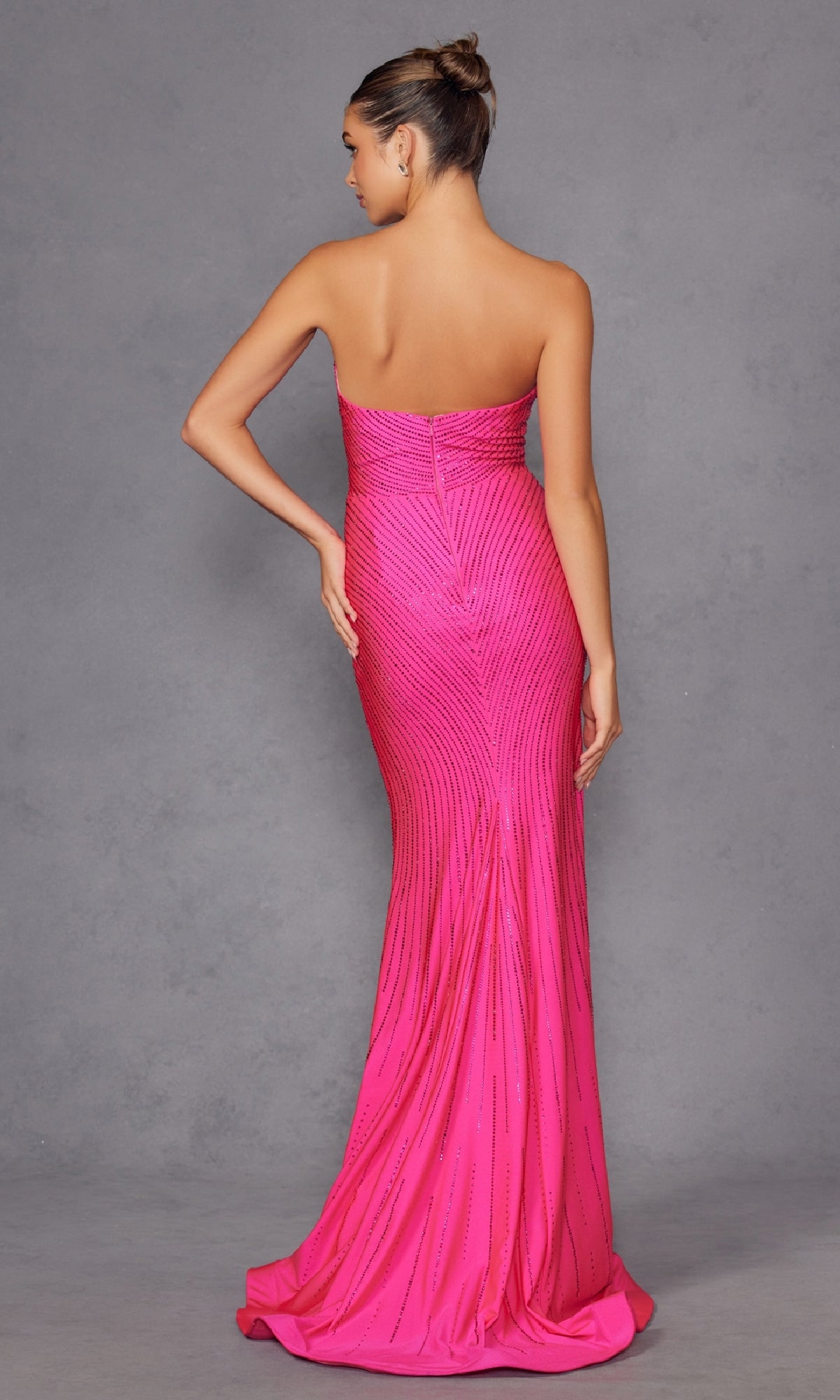 A woman stands with her back to the camera against a plain gray background, wearing the Juliet JT2472R Strapless Long Sequin Prom Dress featuring a fitted, floor-length pink silhouette with subtle vertical detailing.