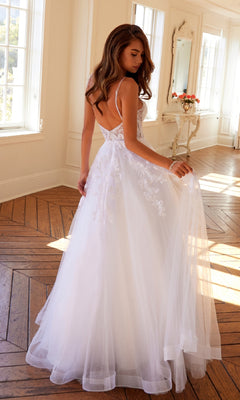 Woman wearing the Long Off-White Prom Dress: Juliet JT2482SW with lace details, a flowing tulle A-line skirt, and a low back, standing on a wooden floor in a bright, elegantly decorated room.