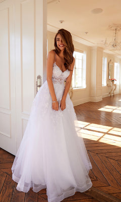 A woman smiles indoors on a wooden floor, wearing the Long Off-White Prom Dress: Juliet JT2482SW and holding her hands together.