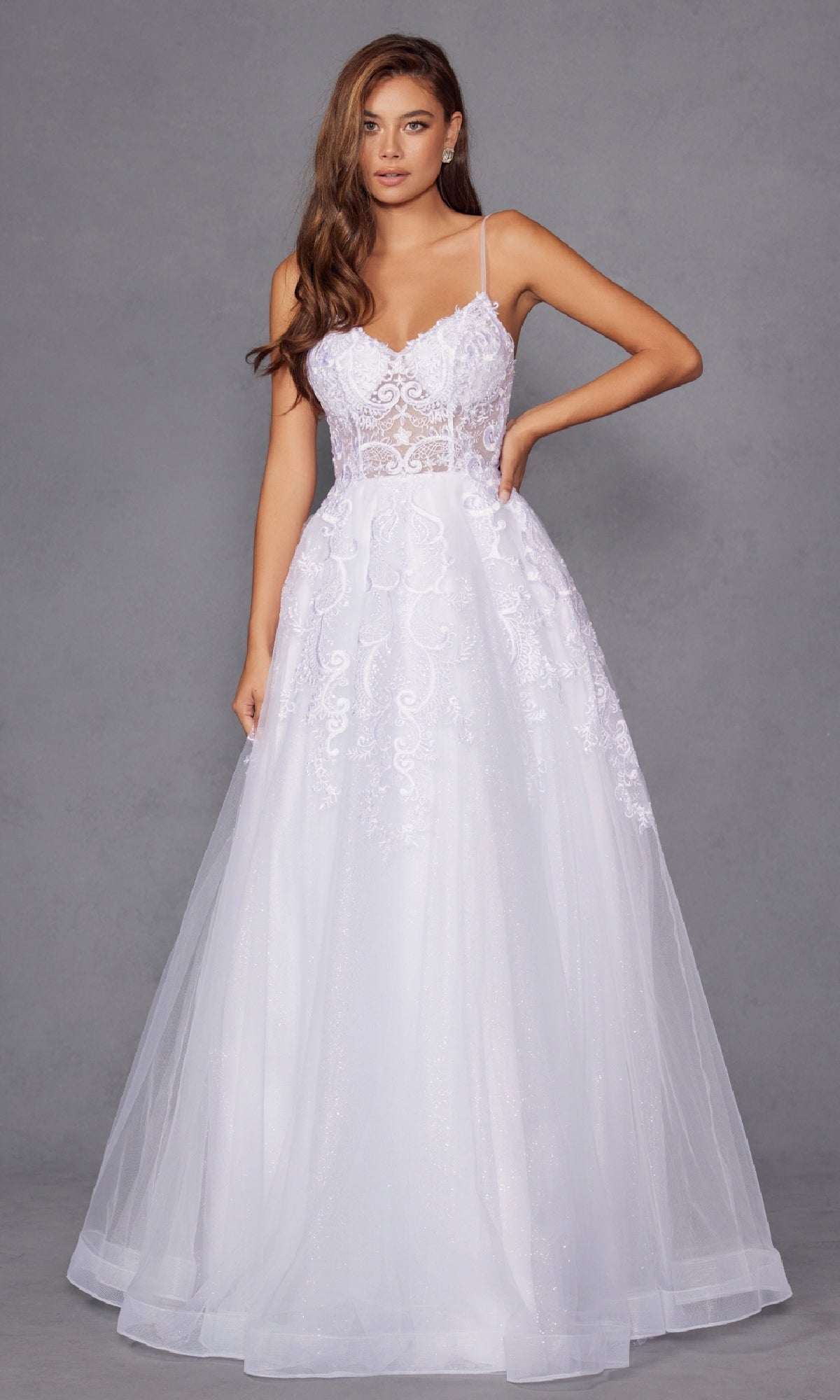 A woman models the Long Off-White Prom Dress: Juliet JT2482SW, featuring a lace bodice with thin straps, sheer details, and a flowing tulle A-line skirt. The sleeveless, fitted gown has a full floor-length silhouette against a plain gray backdrop.