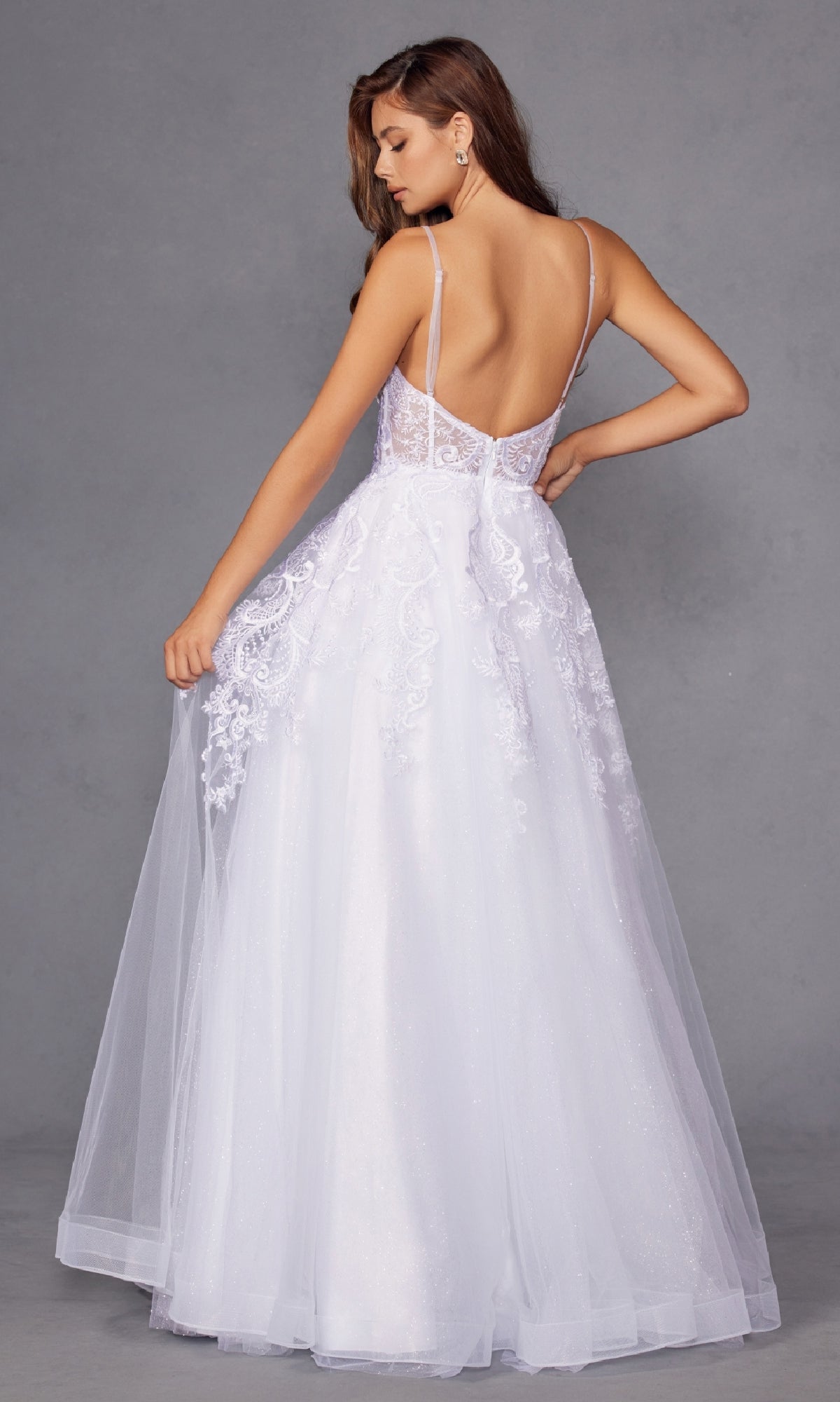 A woman models the Long Off-White Prom Dress Juliet JT2482SW, featuring a lace bodice, sheer straps, and a flowing tulle A-line skirt, standing against a plain gray background.