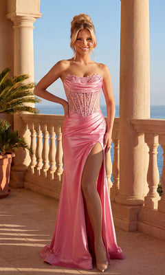 A woman in a candy pink Strapless Lace-Bodice Prom Dress: PromGirl Exclusive, featuring a lace bodice and high side slit, stands on a balcony overlooking the sea, framed by elegant columns and lush potted plants.