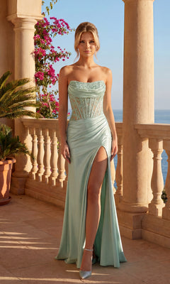 A woman stands on a sunlit terrace by the sea, wearing a sage Strapless Lace-Bodice Prom Dress: PromGirl Exclusive with a high side slit and lace detailing. Pink flowers and elegant columns complete the romantic scene.
