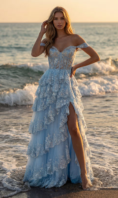 A woman stands barefoot on a beach at sunset, wearing the PromGirl 250005 A-Line Corset Lace Prom Dress with off-the-shoulder ruffles and a high slit. Gentle waves roll in the background.