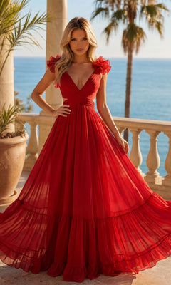 A woman in a red Long Prom Dress with Ruffle Straps (PromGirl Exclusive) stands on a balcony overlooking the sea, with palm trees and a clear blue sky in the background.