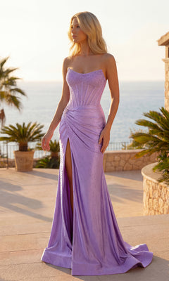 A woman stands outdoors by palm trees and a stone wall, wearing the lilac Sparkly Long Corset Prom Dress: PromGirl Exclusive 250044, featuring a strapless design, fitted bodice, and side slit. The sea glimmers in the background.