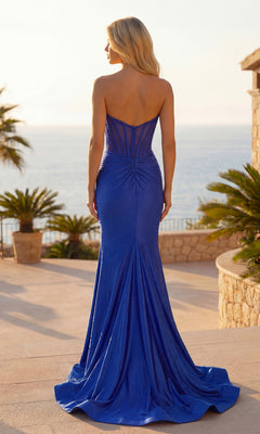 A woman stands outdoors with her back to the camera, wearing the Sparkly Long Corset Prom Dress: PromGirl Exclusive 250044 in royal blue, overlooking a seaside view with palm trees and stone structures.