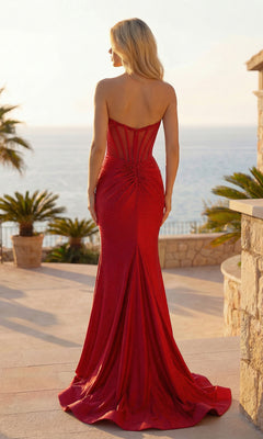 A woman in the Sparkly Long Corset Prom Dress: PromGirl Exclusive 250044 stands outdoors on a terrace, facing the ocean with palm trees and stone railings in the background.