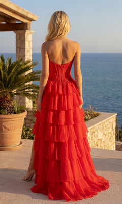 A woman in the PromGirl Exclusive 250267 Ruffled Long Prom Dress stands on a terrace with ocean views, surrounded by stone walls and potted plants.