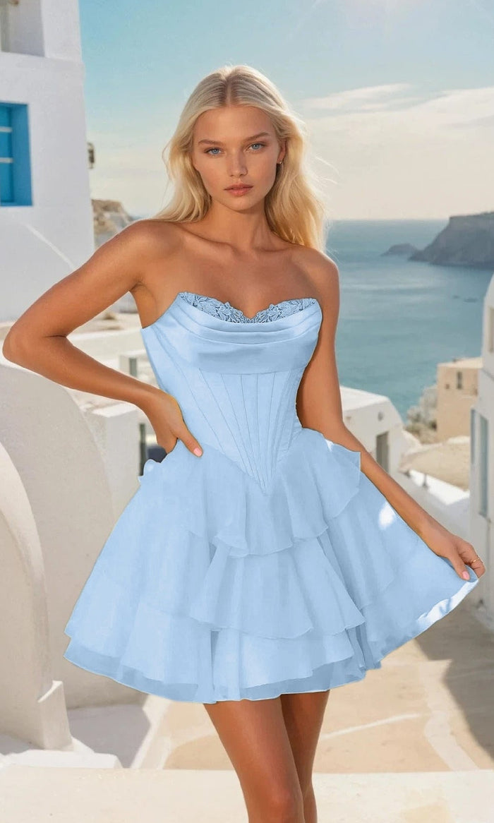 Woman in a light blue short dress standing in a picturesque Mediterranean setting with white buildings and blue sky.