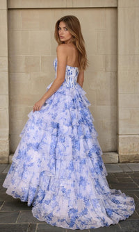 Woman in a blue floral dress standing against a stone wall.