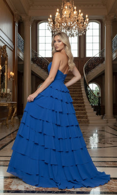 Wearing the Long Prom Dress: Poly USA 25012—with a strapless chiffon design, sweetheart neckline, and tiered A-line skirt—a woman stands in an elegant marble-floored foyer with a chandelier and staircase.