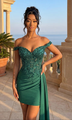 A woman in the Off-Shoulder Hoco Dress: PromGirl Exclusive 250138 stands on a balcony with ornate columns, her green sequined gown sparkling as she gazes over a scenic, sunlit landscape.