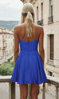 Woman showing the back of a short blue dress as she stands on a balcony with a scenic view in the background