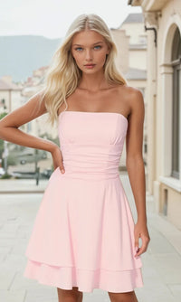 Woman wearing a short light pink strapless dress standing outdoors with a blurred background.