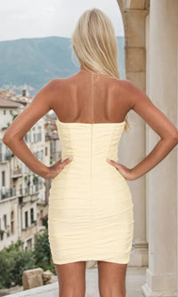 Woman showing the back of a light yellow ruched homecoming dress that she's wearing while looking off a balcony.