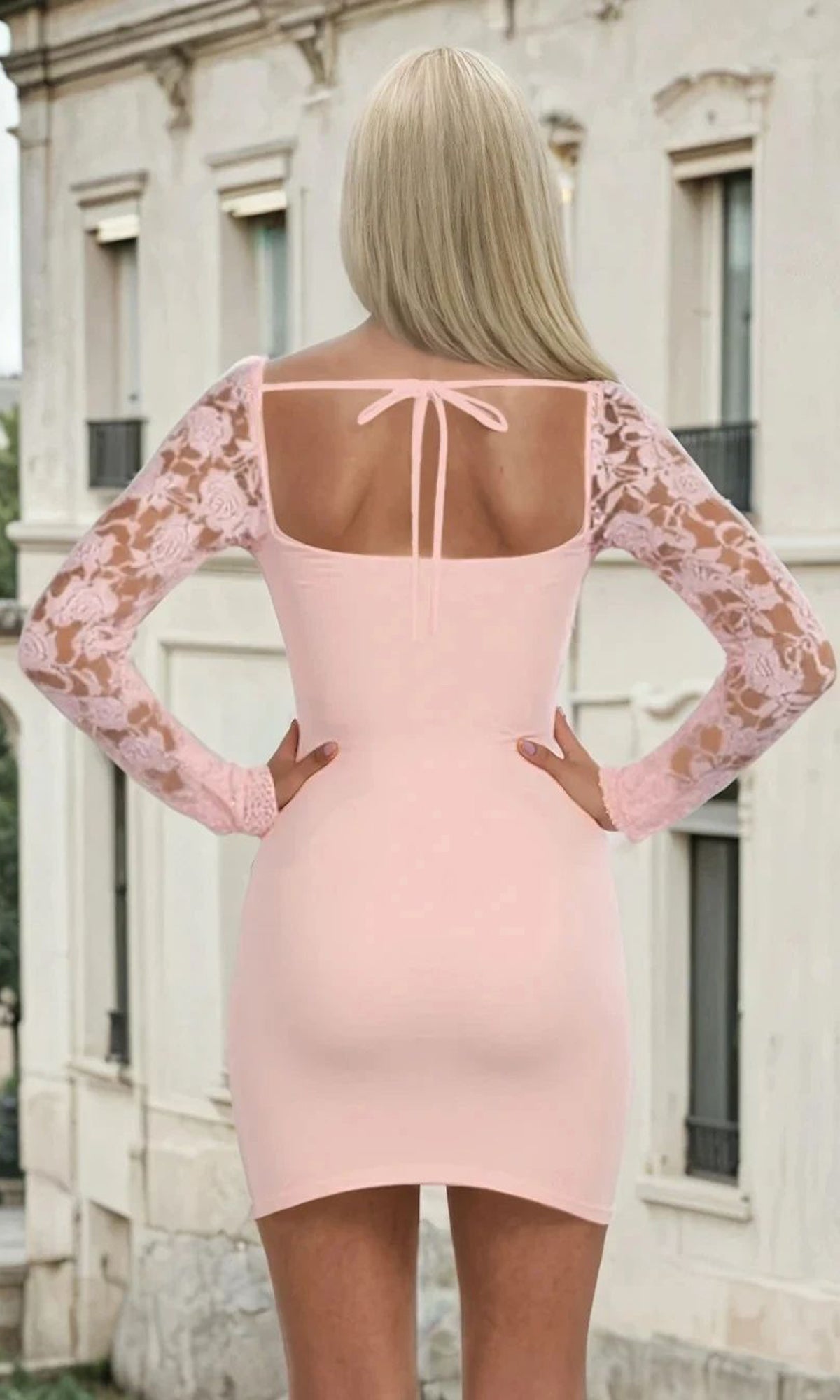 Pink dress with lace sleeves and open back back design, worn by a woman in an urban setting.